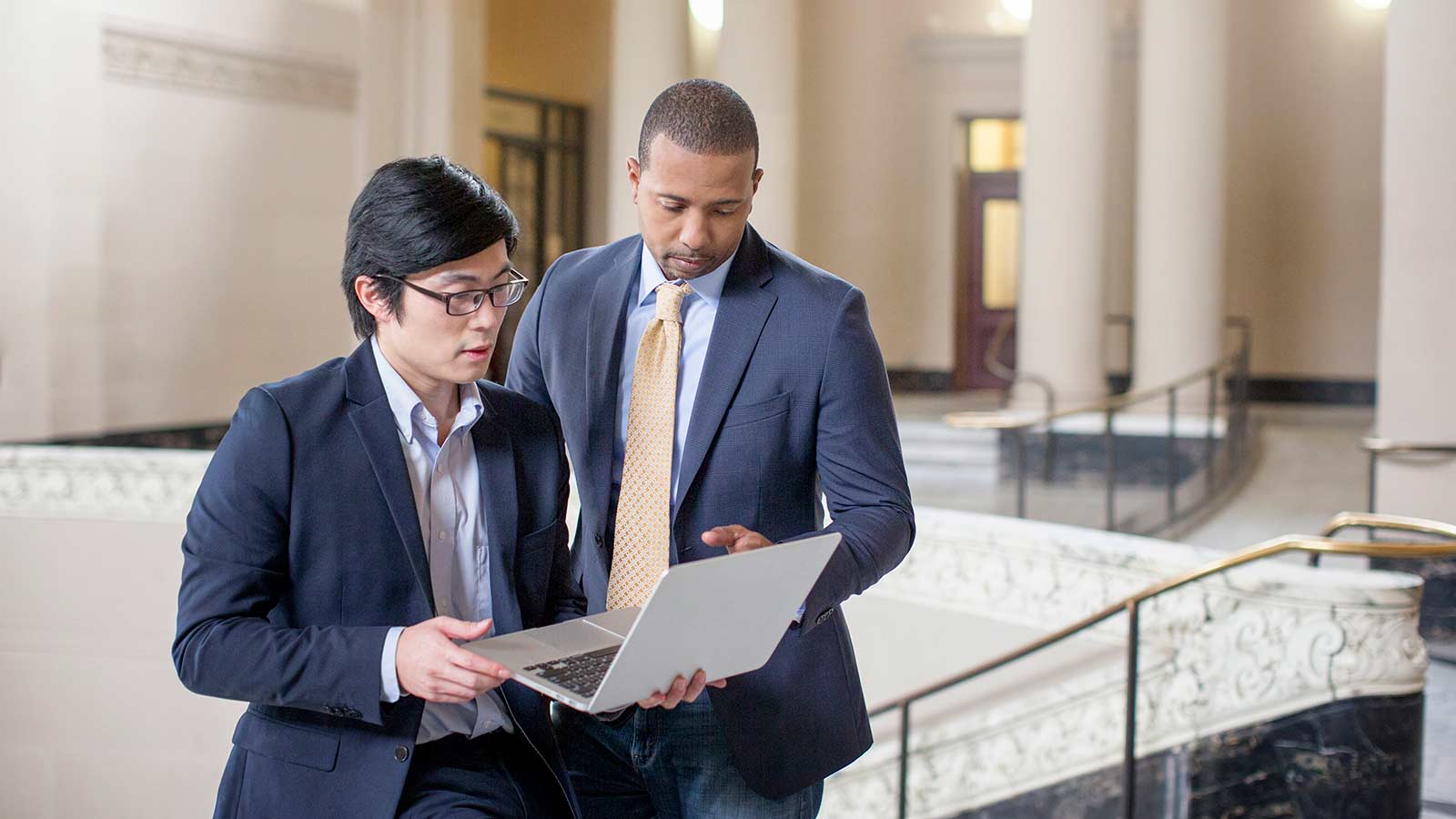Two business men standing and conversing while looking at a laptop.